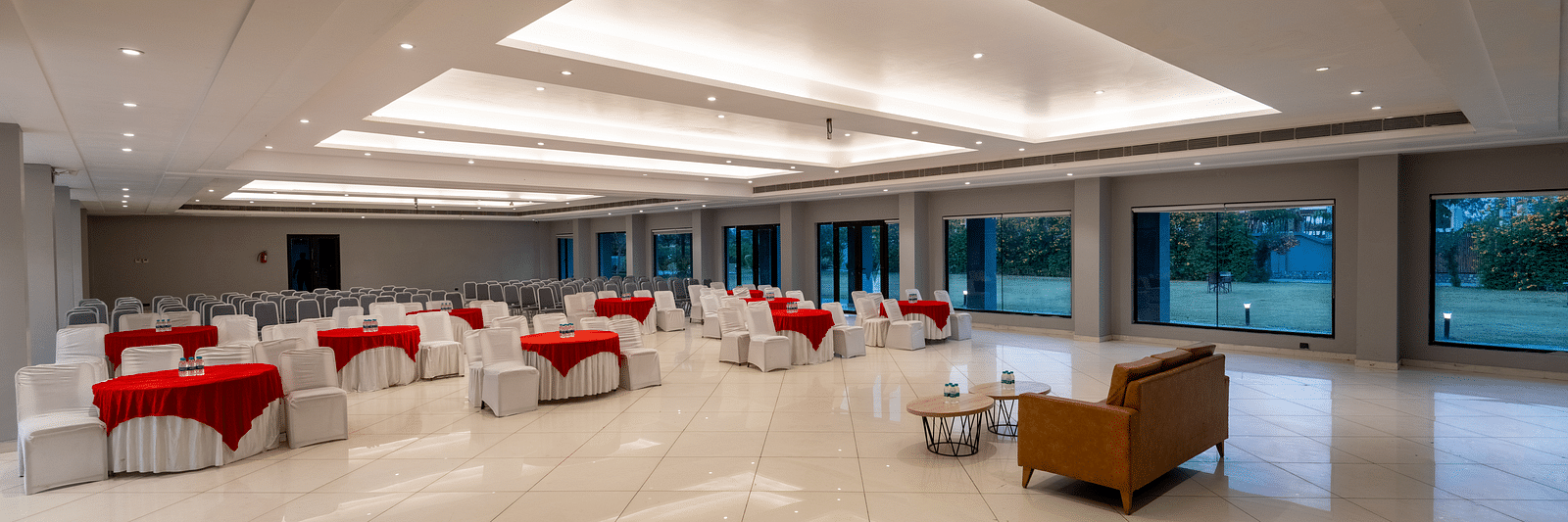 Side view of tables with neatly decorated tablecloths, a plush sofa, and two round tables set in front at DLS Forest Vines Resort.